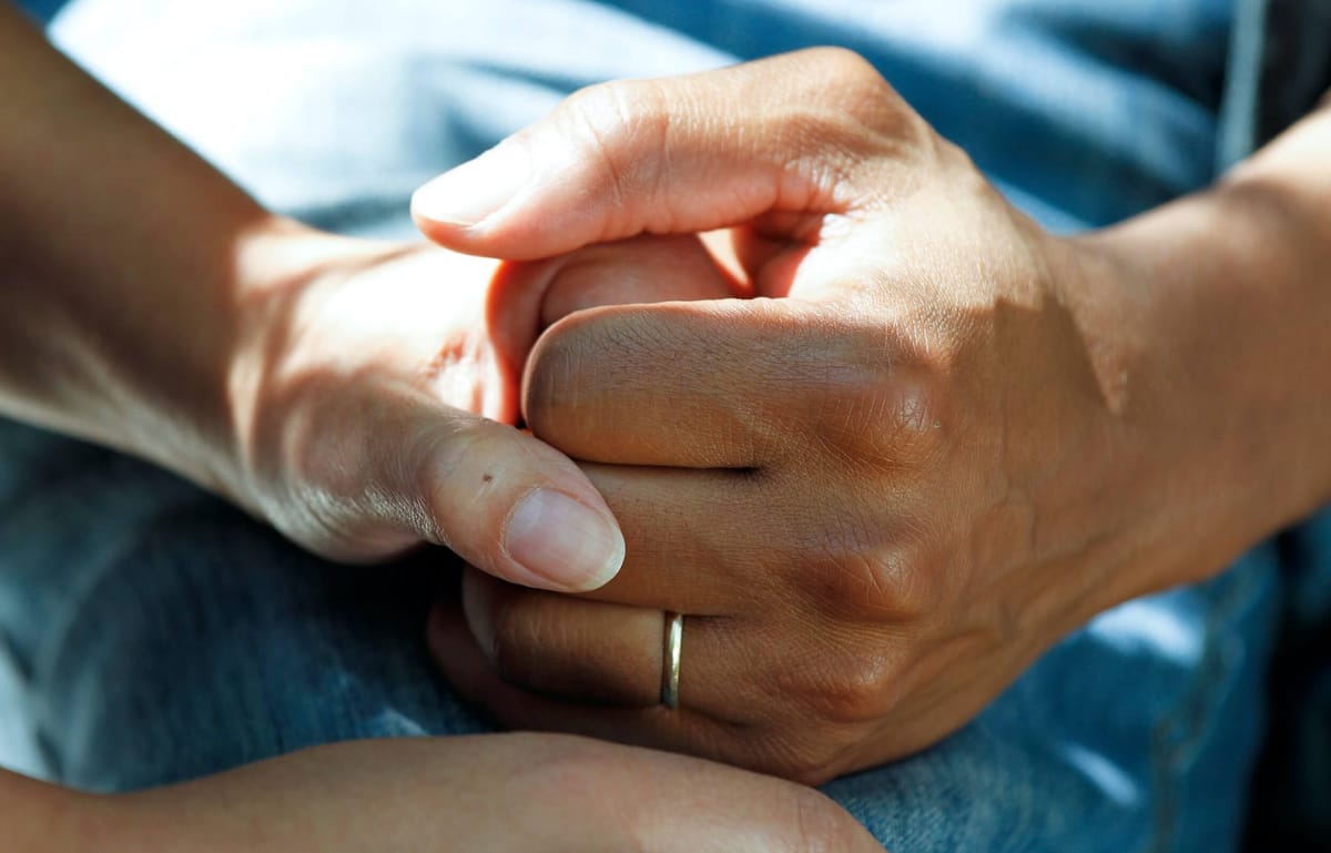 Close-up photo of hands holding, one of which is wearing a wedding ring.
