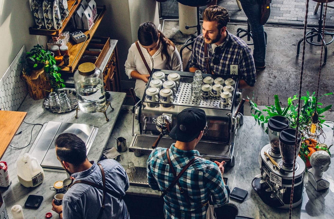 A pair of baristas preparing coffee in a coffee shop while a man and woman wait on the other side of the counter.