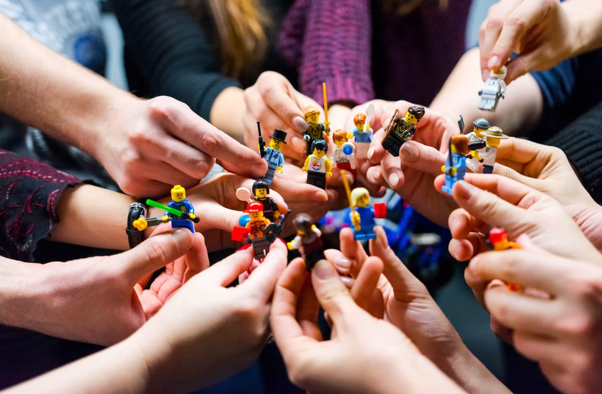 Many hands holding tiny Lego figures in a variety of outfits and holding different tools.